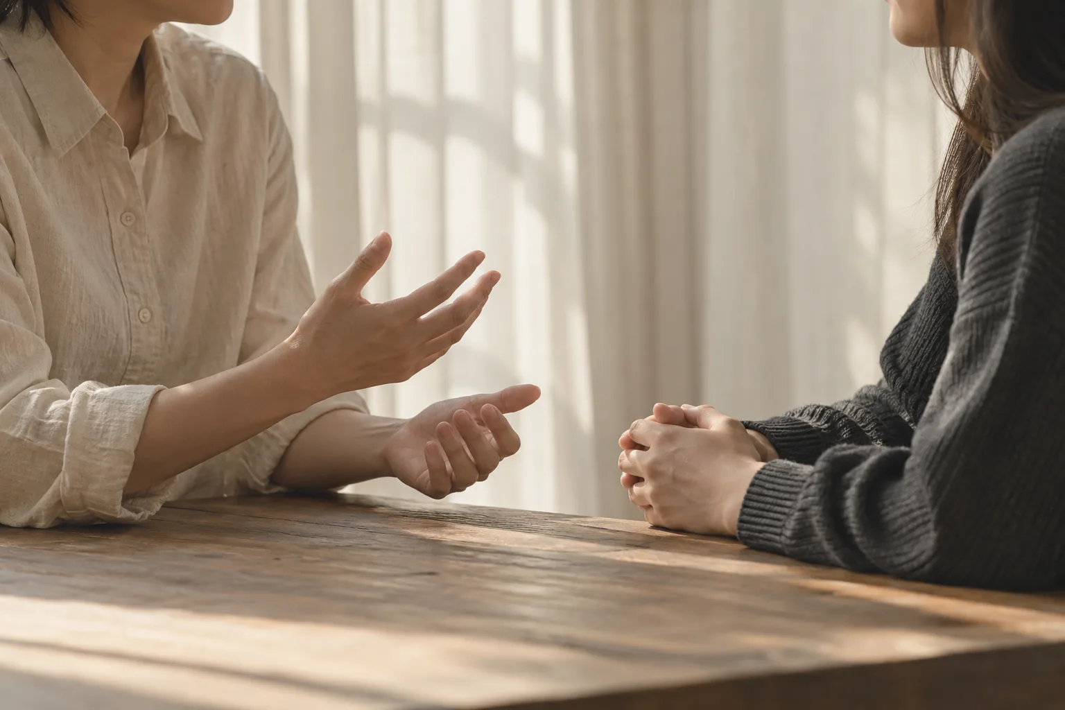 두 사람이 창가에 마주 앉아 자연스럽게 대화하는 모습을 손과 어깨 중심으로 담은 사진